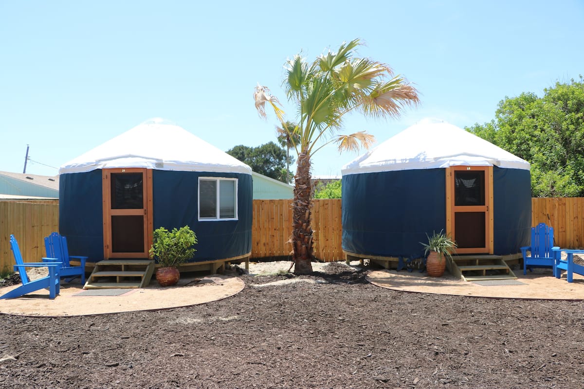 Deux yourtes avec une terrasse en bois, un palmier et des chaises bleues.
