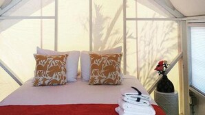 Una habitación tipo tienda de campaña con cama, almohadas y un jarrón con flores.