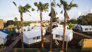 Un camping con varias tiendas blancas, sillas de madera y palmeras.