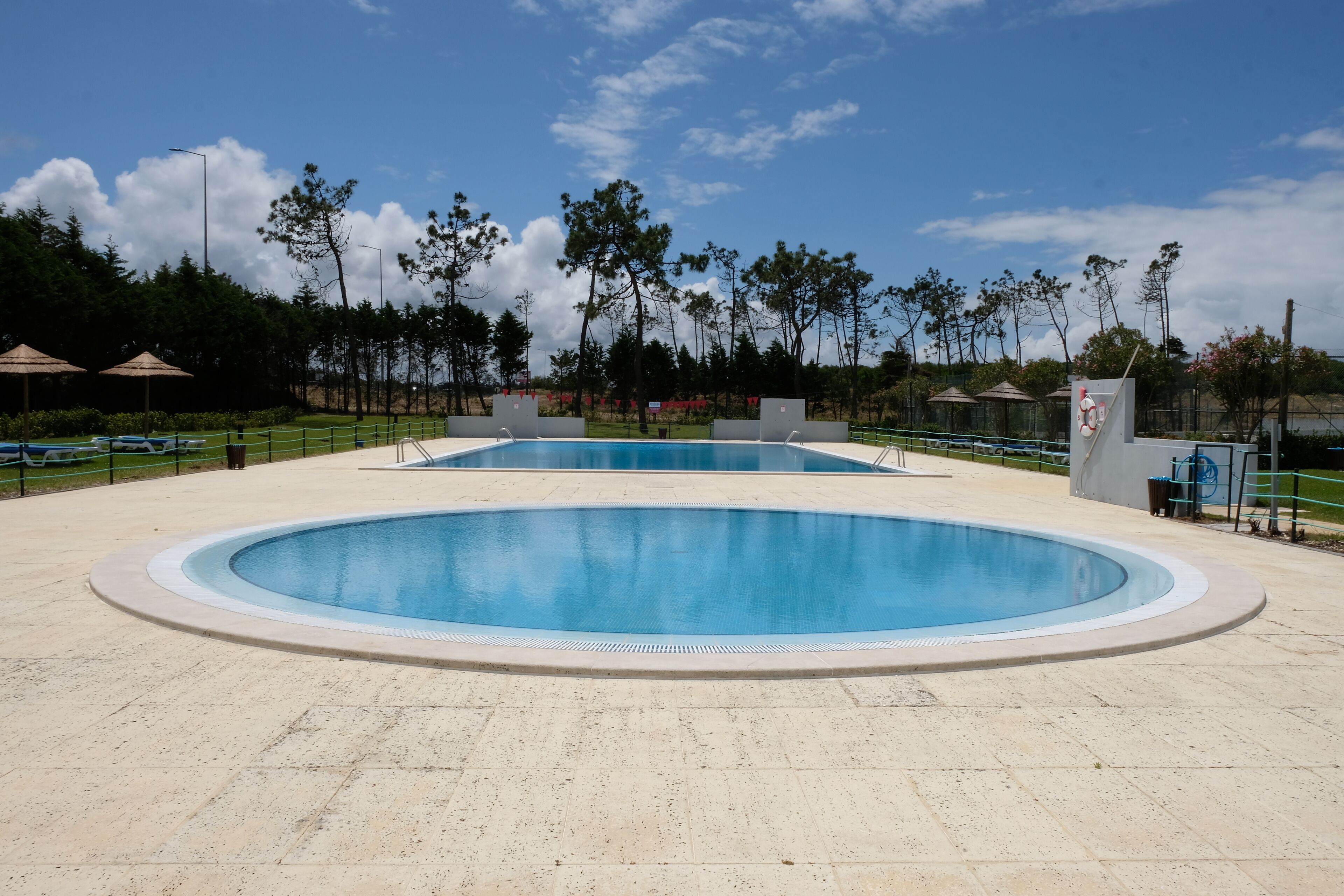 Ein großer Pool im Freien mit einer gefliesten Liegefläche, umgeben von Bäumen und Sonnenschirmen.
