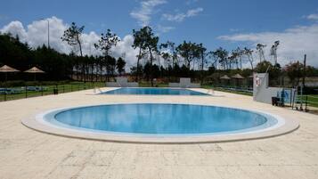 Ein großer Pool im Freien mit einer gefliesten Liegefläche, umgeben von Bäumen und Sonnenschirmen.
