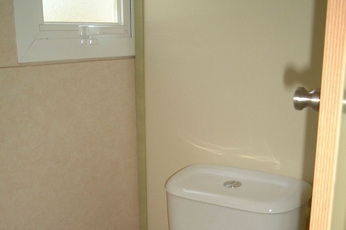 Un baño pequeño con un inodoro blanco en un espacio reducido, paredes color beige y una ventana encima.
