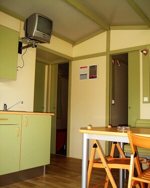 Une cuisine compacte avec un téléviseur fixé au-dessus du comptoir, une table à manger avec des chaises et un petit meuble de rangement.