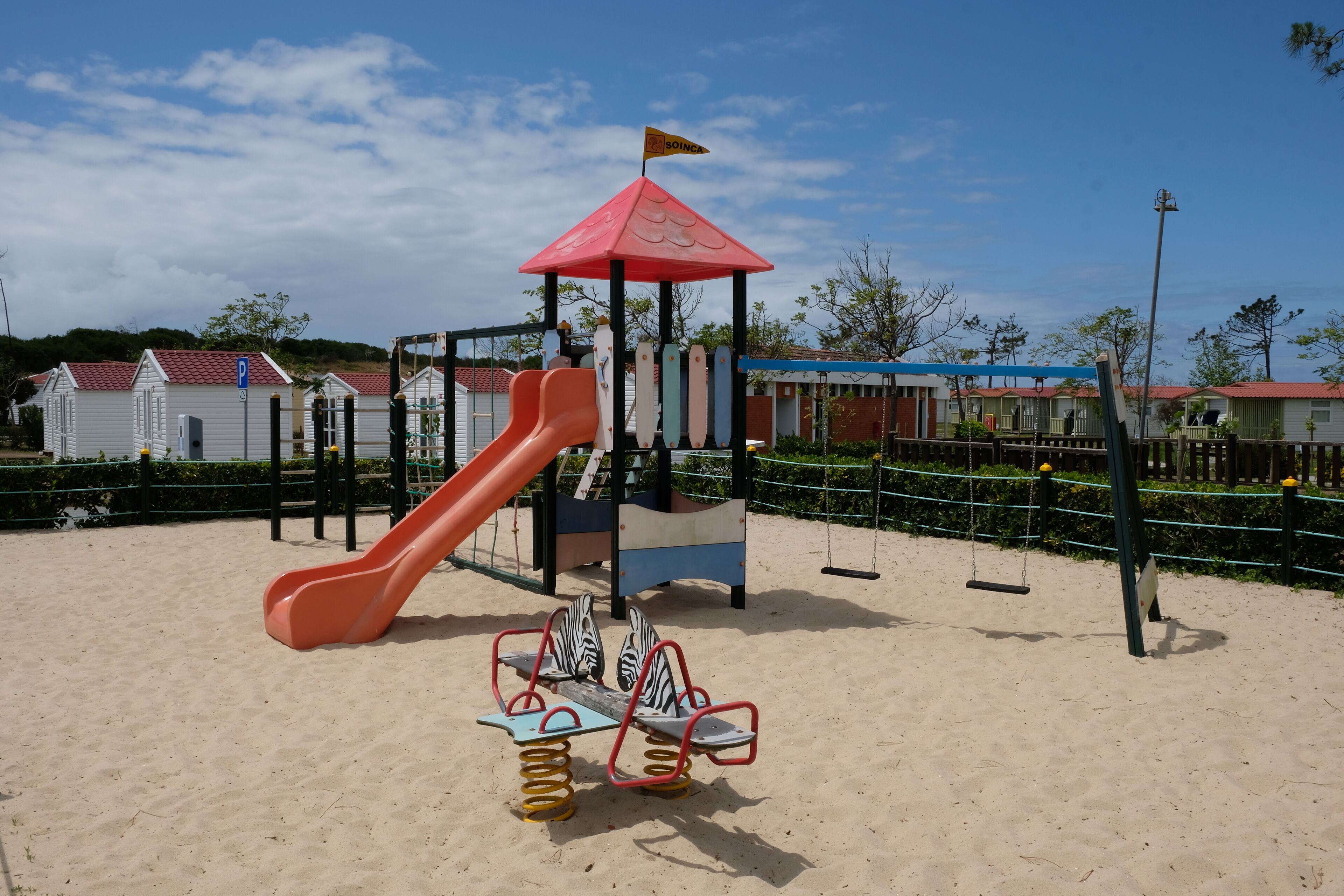 A playground with a slide, swings, and seesaw.