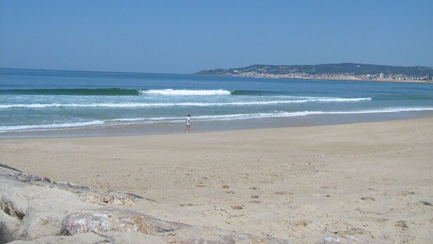 Ein weiter Sandstrand mit sanften Wellen und blauem, wolkenlosem Himmel.