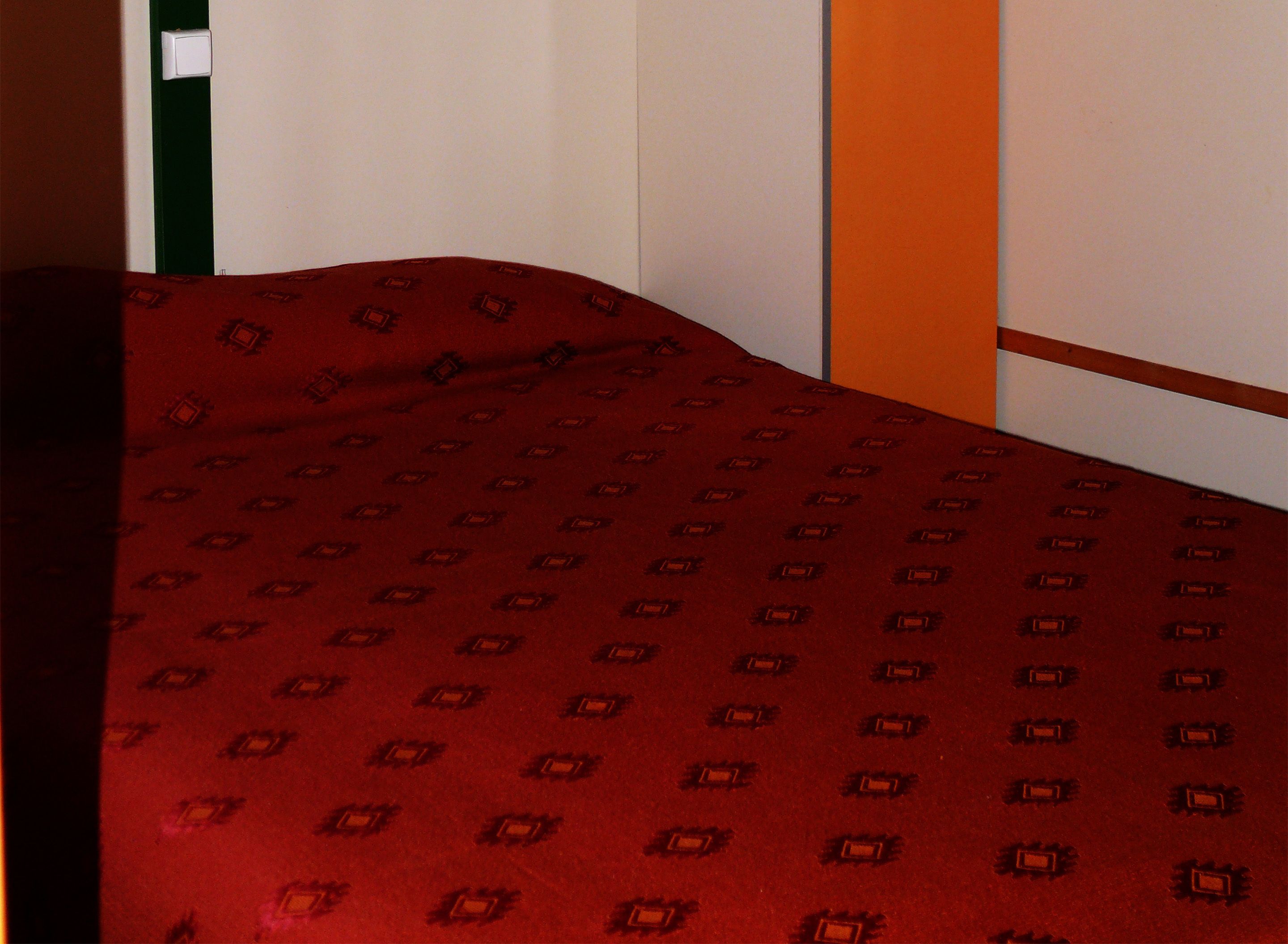 A bed with a red patterned bedspread, a green wall, and an orange accent wall.