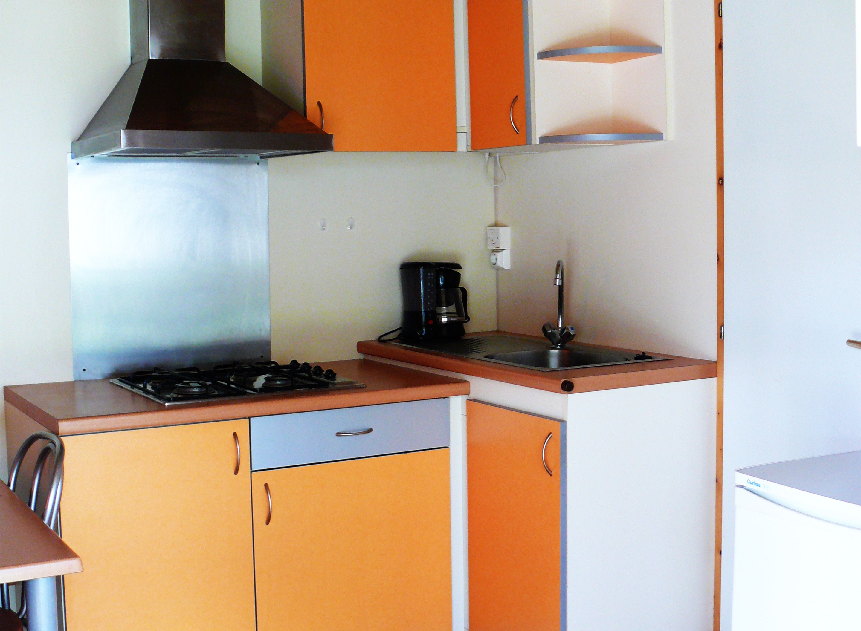 Une cuisine compacte avec des meubles de couleur orange, une hotte de cuisine en acier inoxydable, une machine à café et un évier.