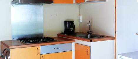 Une cuisine compacte avec des meubles de couleur orange, une hotte de cuisine en acier inoxydable, une machine à café et un évier.