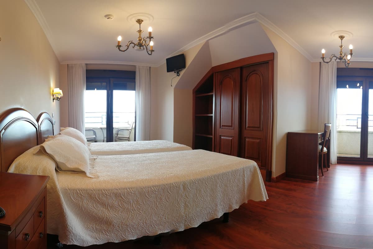 A hotel room with two beds, a wooden wardrobe, a desk, and a chair.