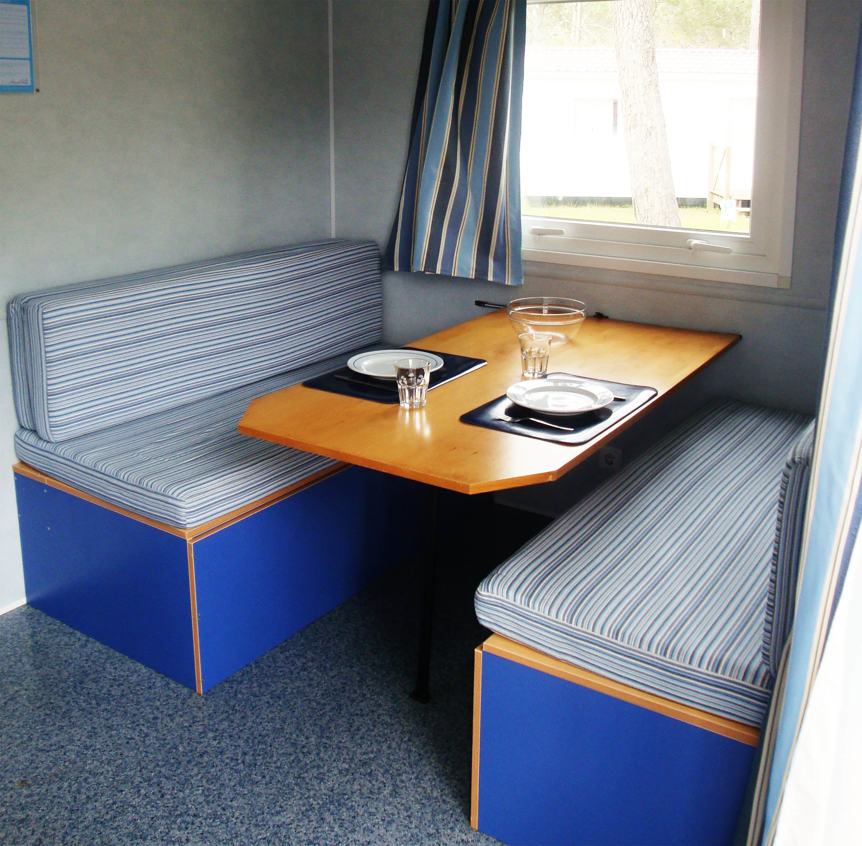 A compact kitchenette with a bench seating area, a small table, and a window with curtains.