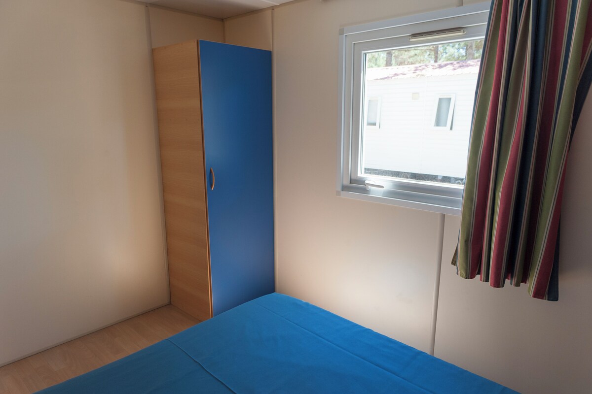 Une chambre avec un lit bleu, une armoire et une fenêtre avec des rideaux.