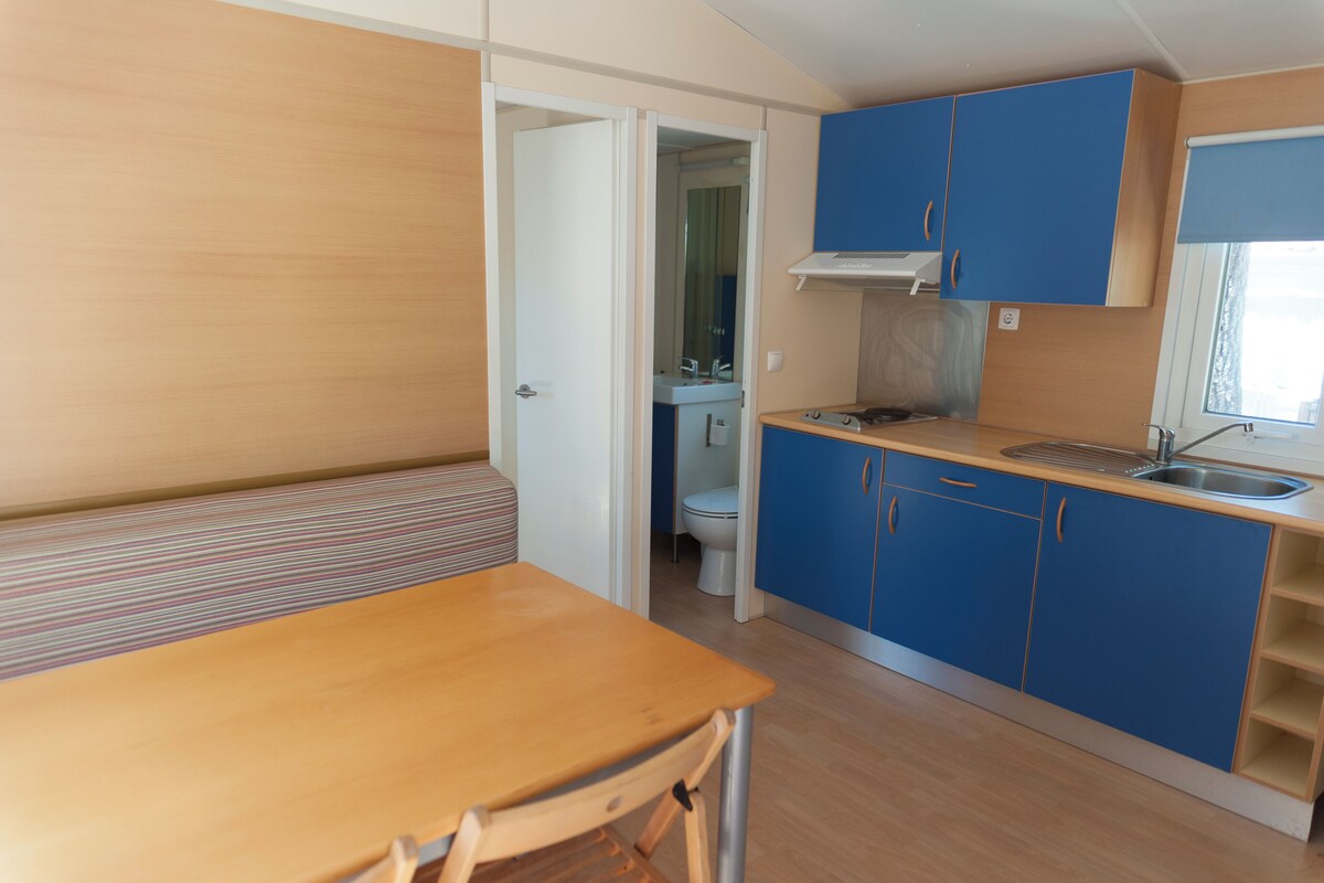 Eine kleine Küche mit Holztisch und blauen Schränken, einem kleinen Spülbecken und einem Fenster mit Jalousien.