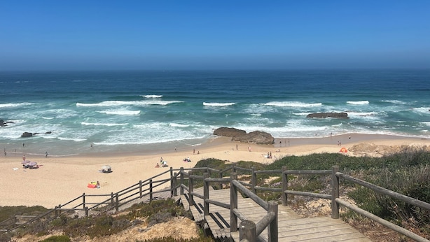 Una escalera de madera que lleva a una playa con gente y sombrillas.