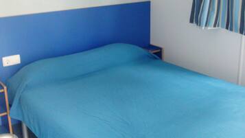 Une chambre avec un lit simple, un mur bleu, une fenêtre avec des rideaux bleus et une petite table de chevet.