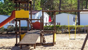 Estructura de madera para jugar con un tobogán y una plataforma, rodeada de arena y árboles.