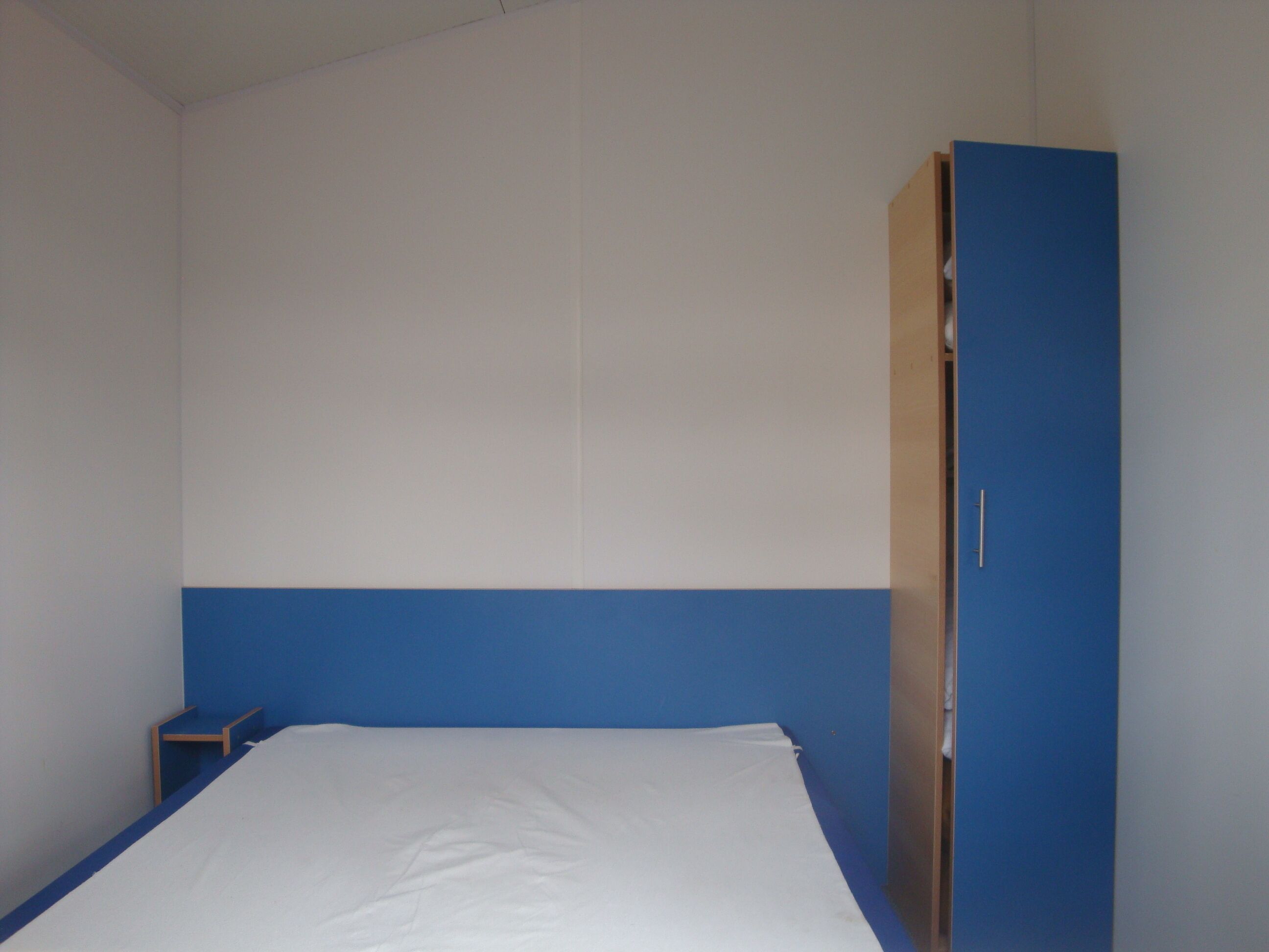 Ein Zimmer mit einem Bett, einem Schrank und einem kleinen Tisch.