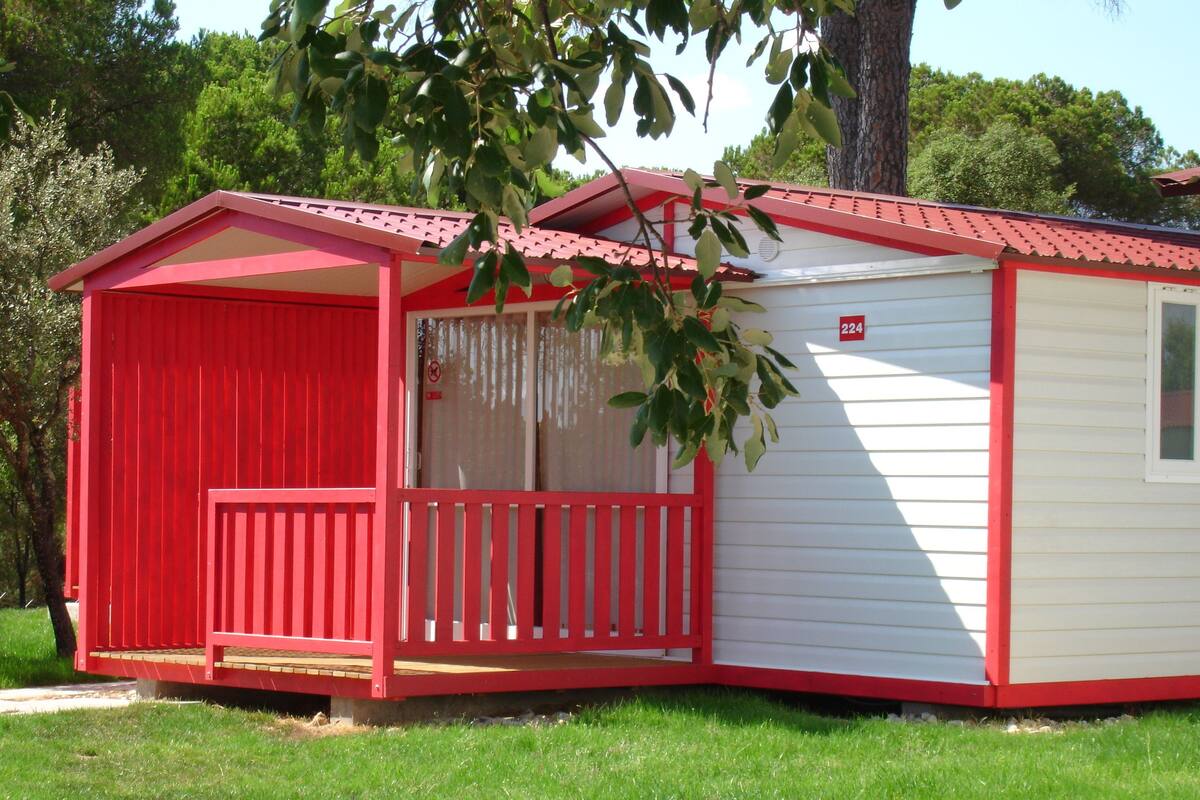A small, single-story building with a red and white exterior, a covered porch, and a small window.