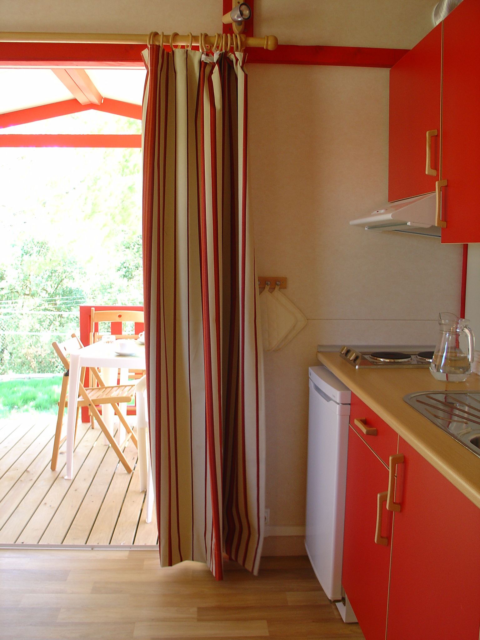 A compact kitchen with a wooden table and chairs, a small refrigerator, and a red cabinet.
