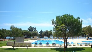 A swimming pool with blue water, surrounded by lounge chairs and trees. - Parque de Campismo Orbitur Montargil (Ponte de Sor)