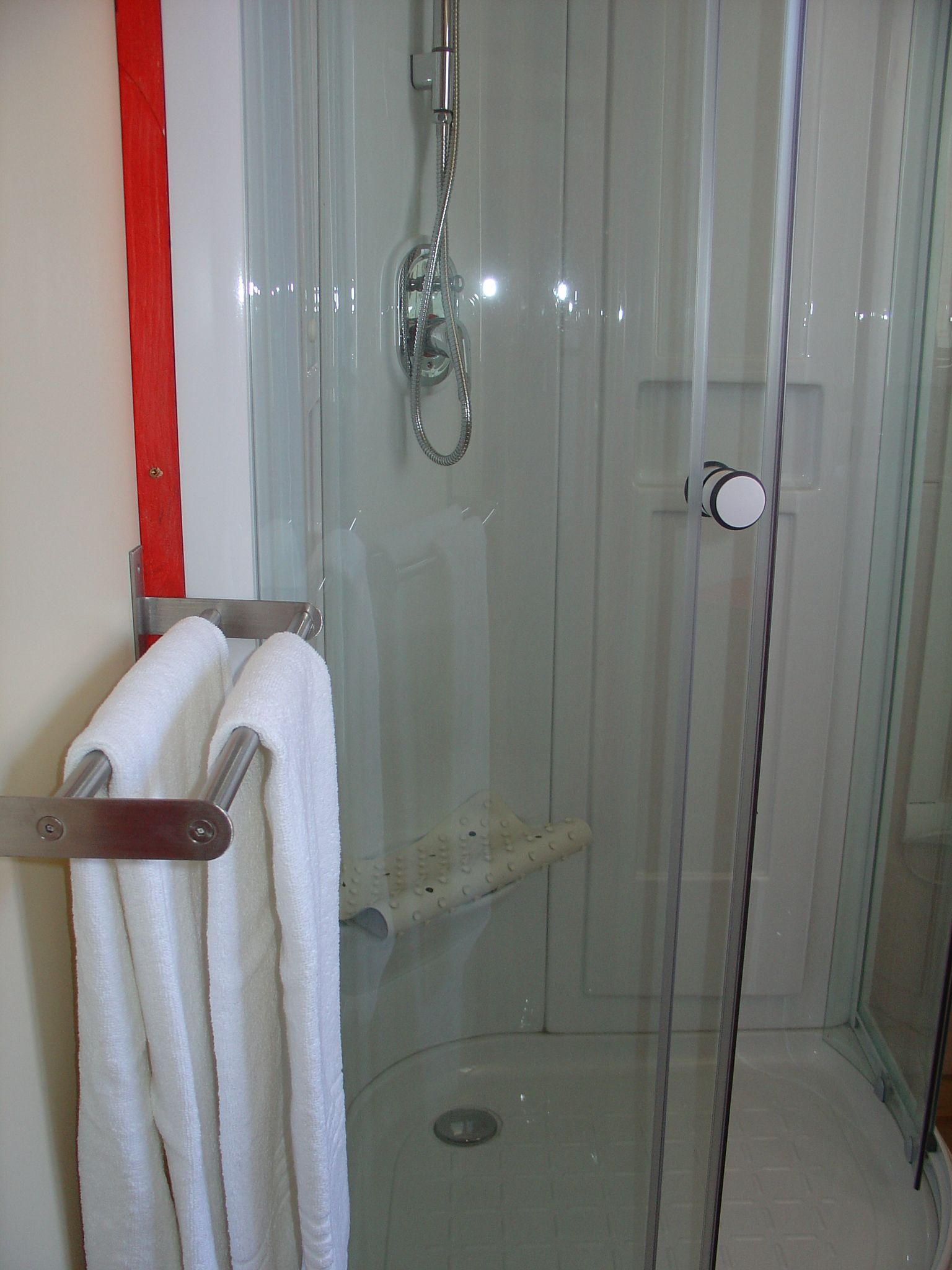 Een douche met glazen wanden, een handdouche, een glazen deur en een handdoekrek met twee witte handdoeken.