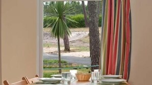A dining area with a table set for two, a bench, and a view of a palm tree and road outside. - Parque de Campismo Orbitur Montargil (Ponte de Sor)