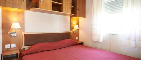 Un dormitorio con cama, armarios de madera, una mesita de noche y una ventana con cortinas.