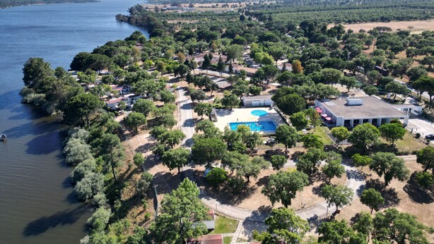 An aerial view of a coastal area with a swimming pool, surrounded by dense greenery and residential buildings. - Parque de Campismo Orbitur Montargil (Ponte de Sor)