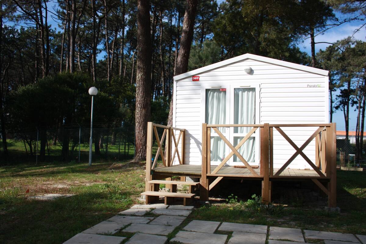 A small, single-story wooden cabin with a number 307 sign, surrounded by trees and a fenced area.