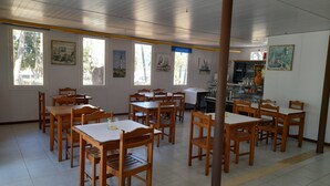 A dining area with wooden tables and chairs, large windows with artwork, and a bar area with shelves. - Parque de Campismo Orbitur Caminha (Caminha)