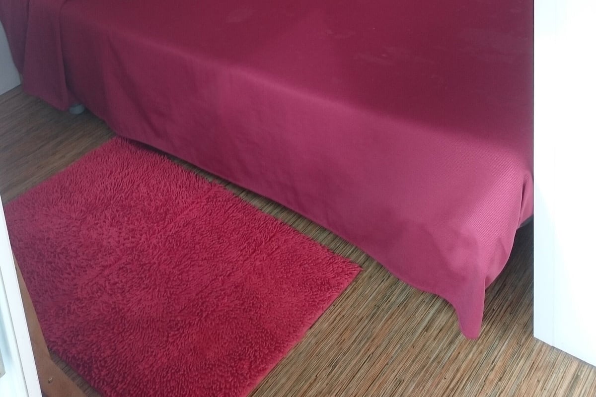 A single bed with a red mattress and orange headboard in a room with white walls and a wooden floor.