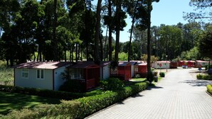A row of small, single-story cabins with red roofs, surrounded by a well-maintained garden and tall trees. - Parque de Campismo Orbitur Caminha (Caminha)