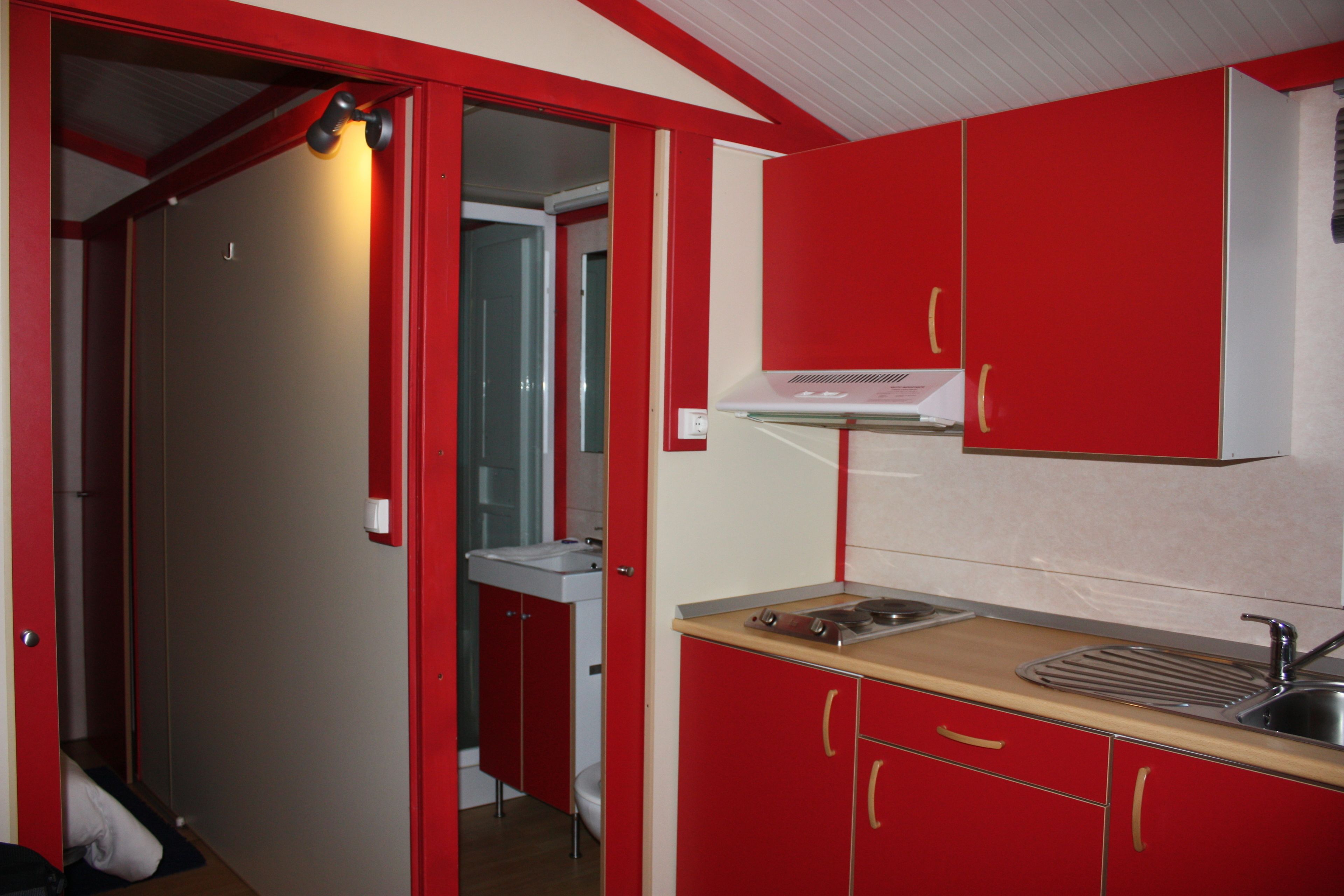 A compact kitchen with red cabinets, a sink, and a stove.