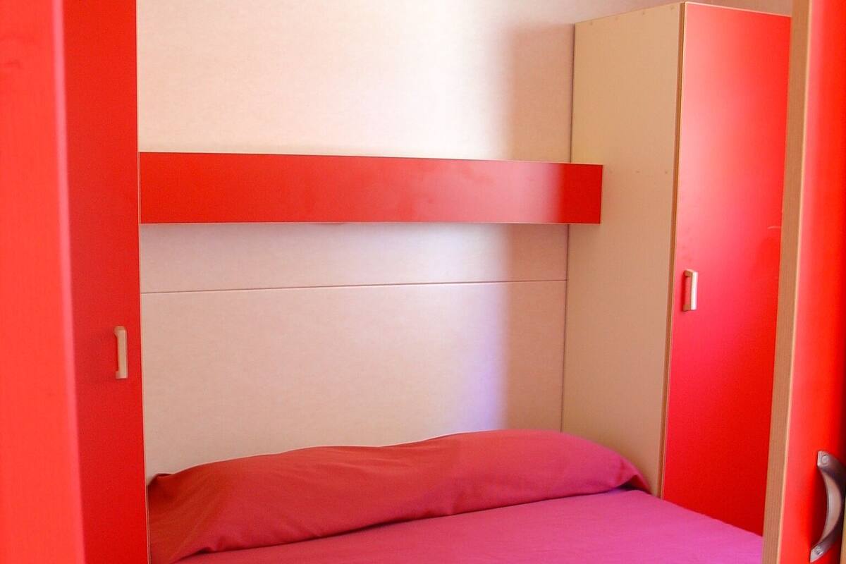 A small, brightly colored room with a bed, a wardrobe, and a door.