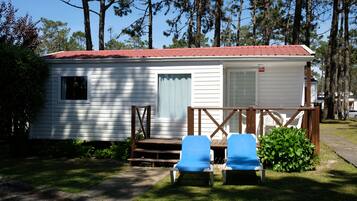 A small white mobile home with a red roof, two blue lawn chairs, and a wooden deck.