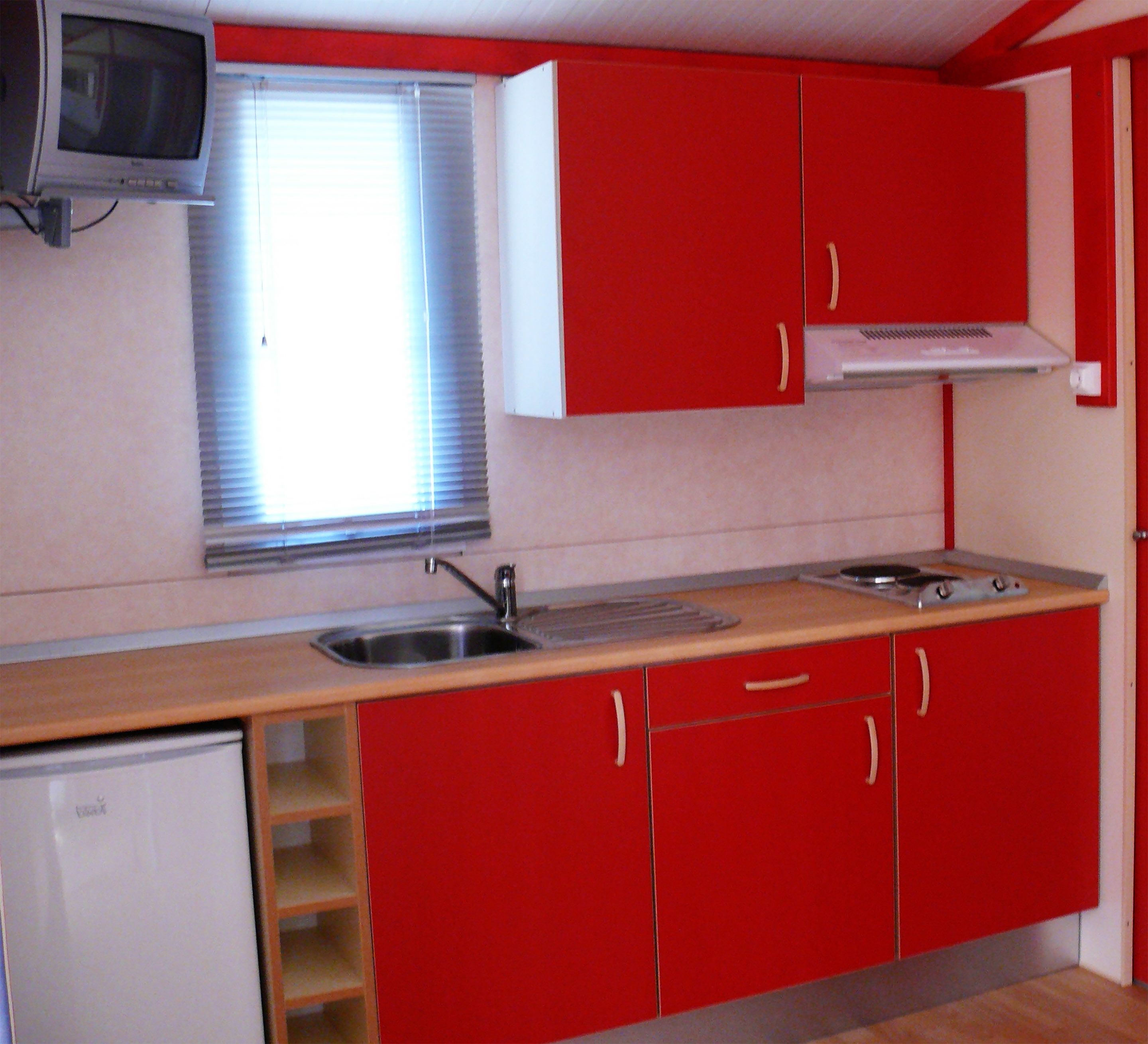 A compact kitchen with red cabinets, a small sink, a microwave, and a window with blinds.
