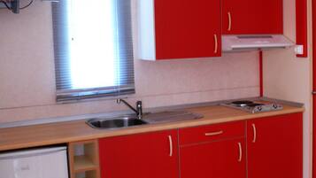 A compact kitchen with red cabinets, a small sink, a microwave, and a window with blinds.