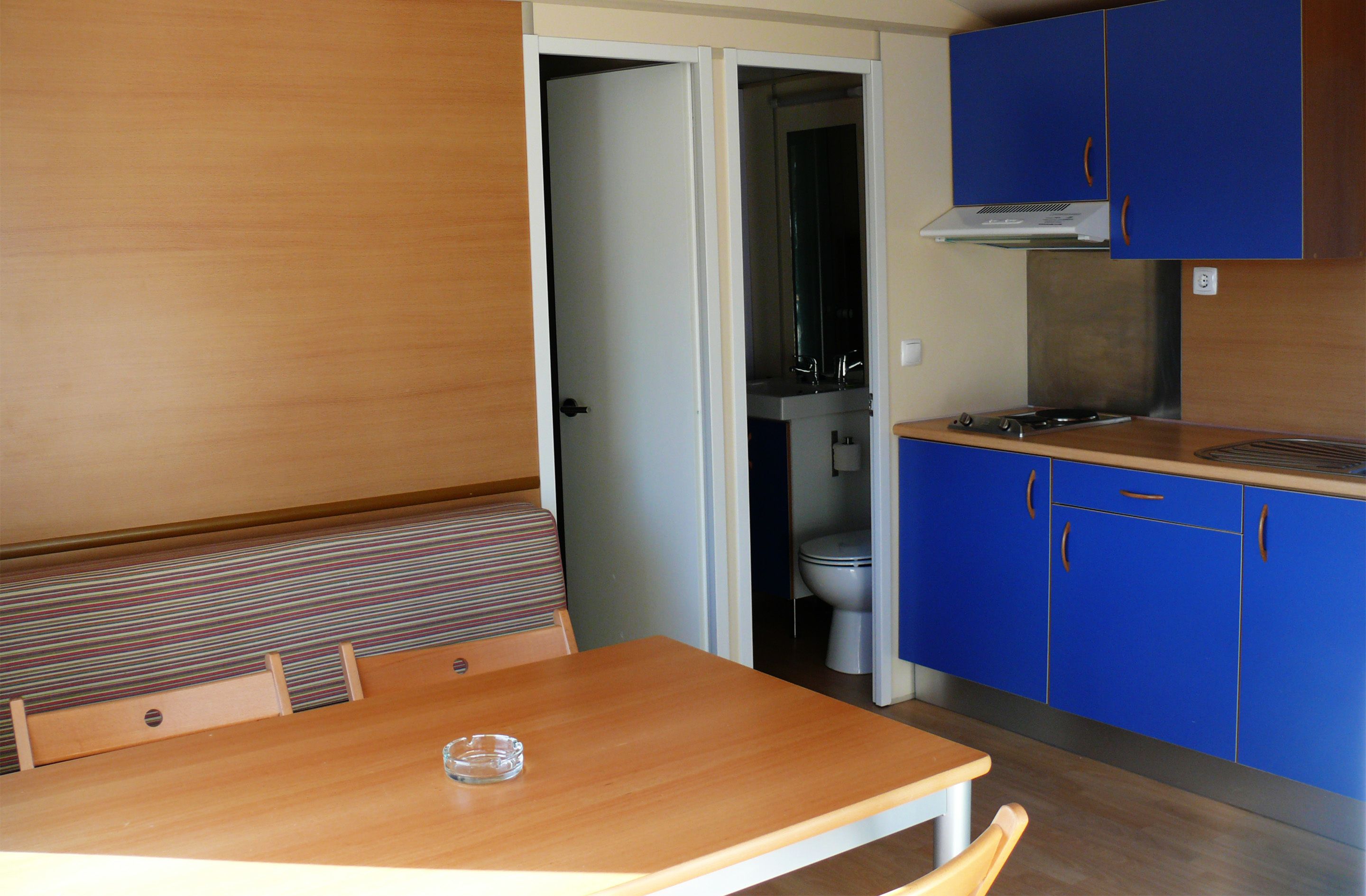 Een kleine keuken met blauwe kastjes, een houten eettafel en een gestreepte bank.