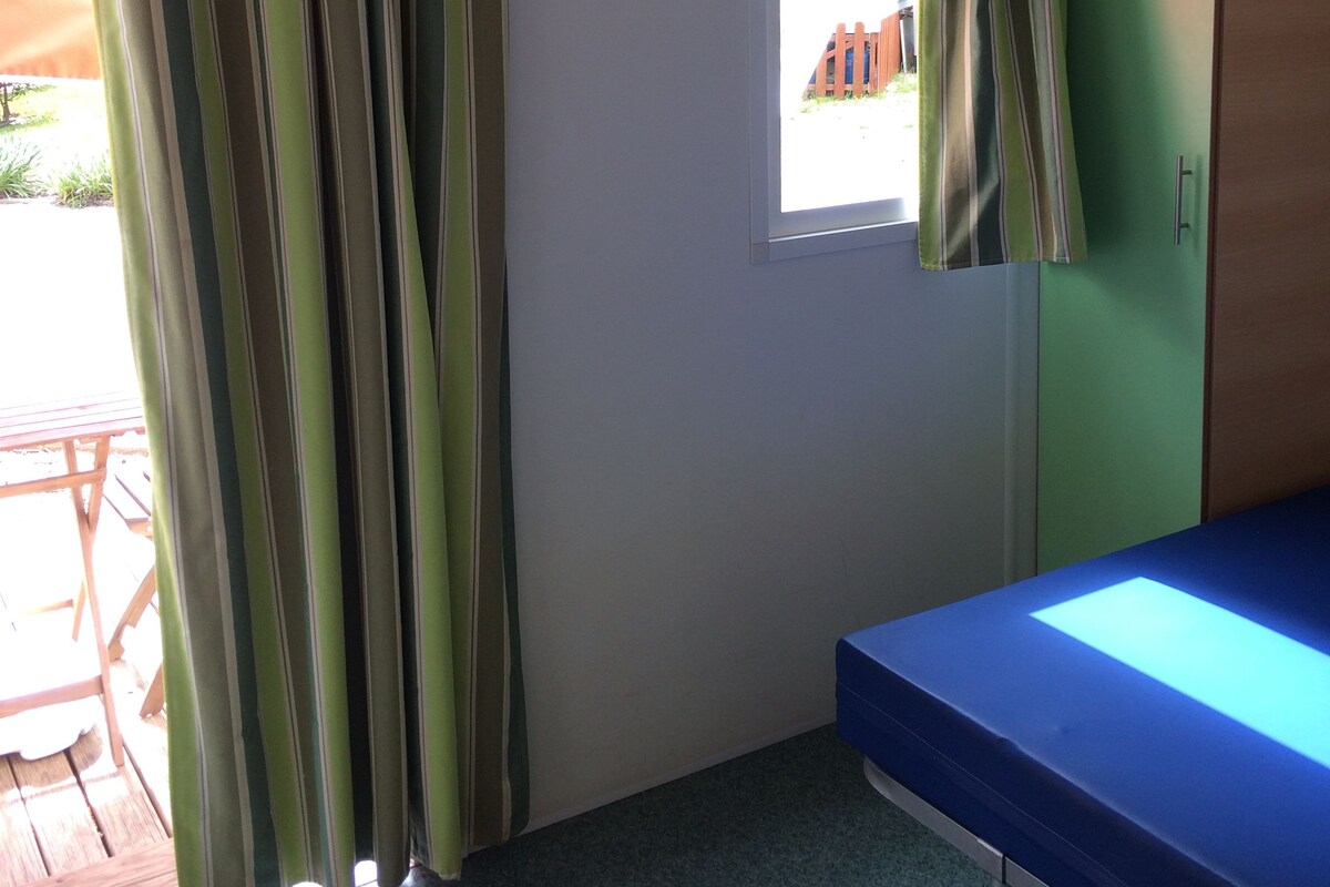 Une chambre avec un lit, un appareil de climatisation, une fenêtre avec des rideaux et une vue sur l’extérieur.