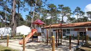 A playground with a slide and climbing structures, surrounded by trees and a building labeled "SUPERMERCADO". - Parque de Campismo Orbitur Sao Pedro De Moel (Marinha Grande)