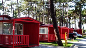 A row of red mobile homes with a grassy area in front, a paved path, and trees in the background. - Parque de Campismo Orbitur Sao Pedro De Moel (Marinha Grande)