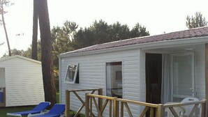 A small white cabin with a deck, two blue lounge chairs, and a wooden staircase leading to a glass door. - Parque de Campismo Orbitur Sao Pedro De Moel (Marinha Grande)