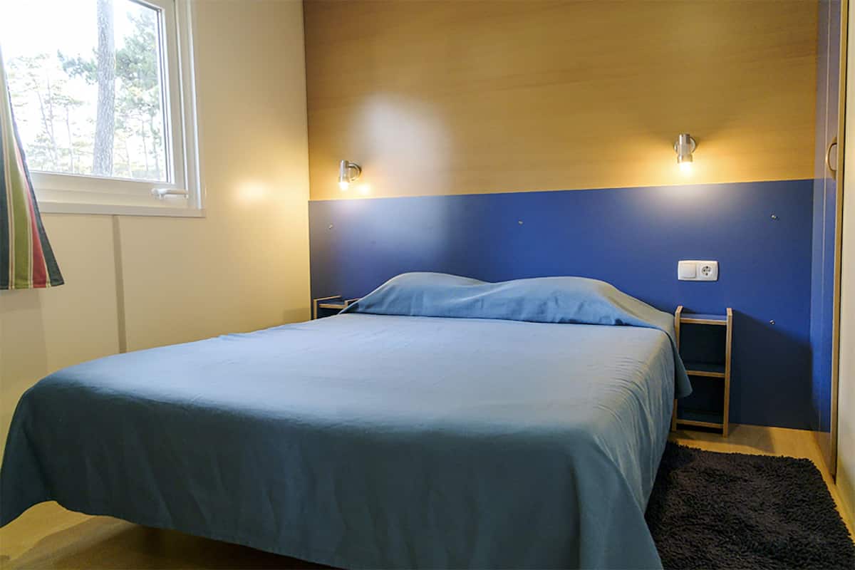 A bedroom with a bed, a window, and a wall-mounted light fixture.
