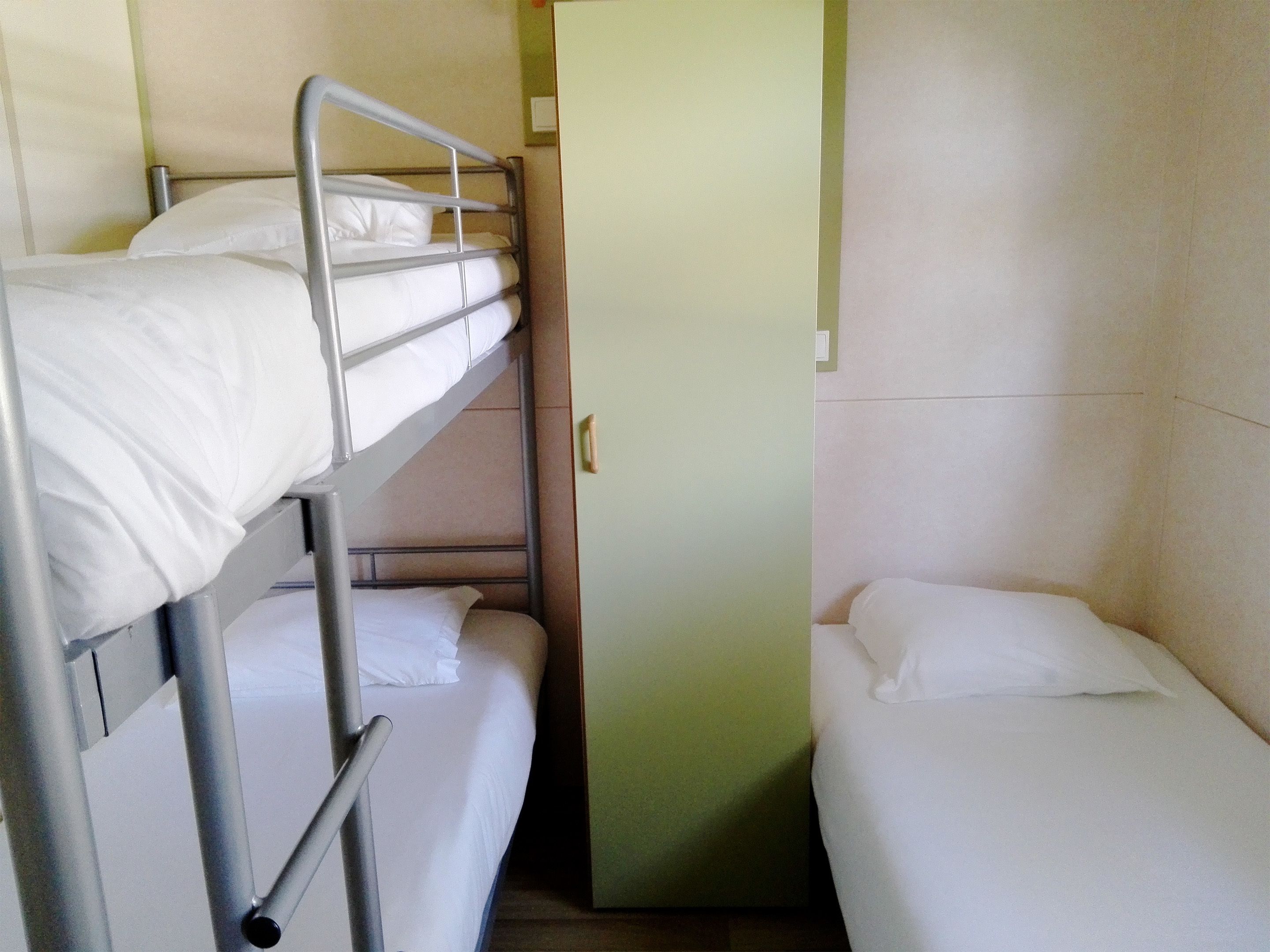 Une chambre avec un lit superposé, un lit simple à droite et le lit du bas à gauche.