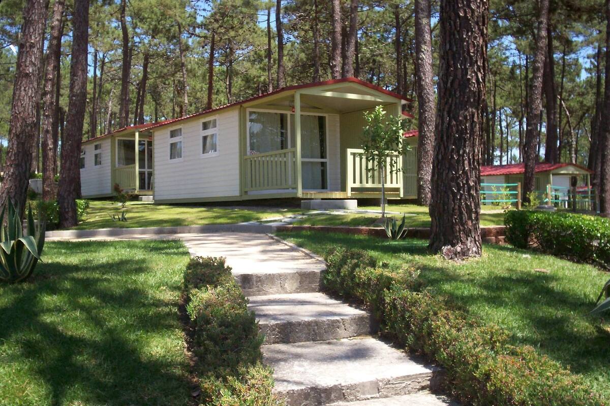 A single-story mobile home with a porch, surrounded by trees.