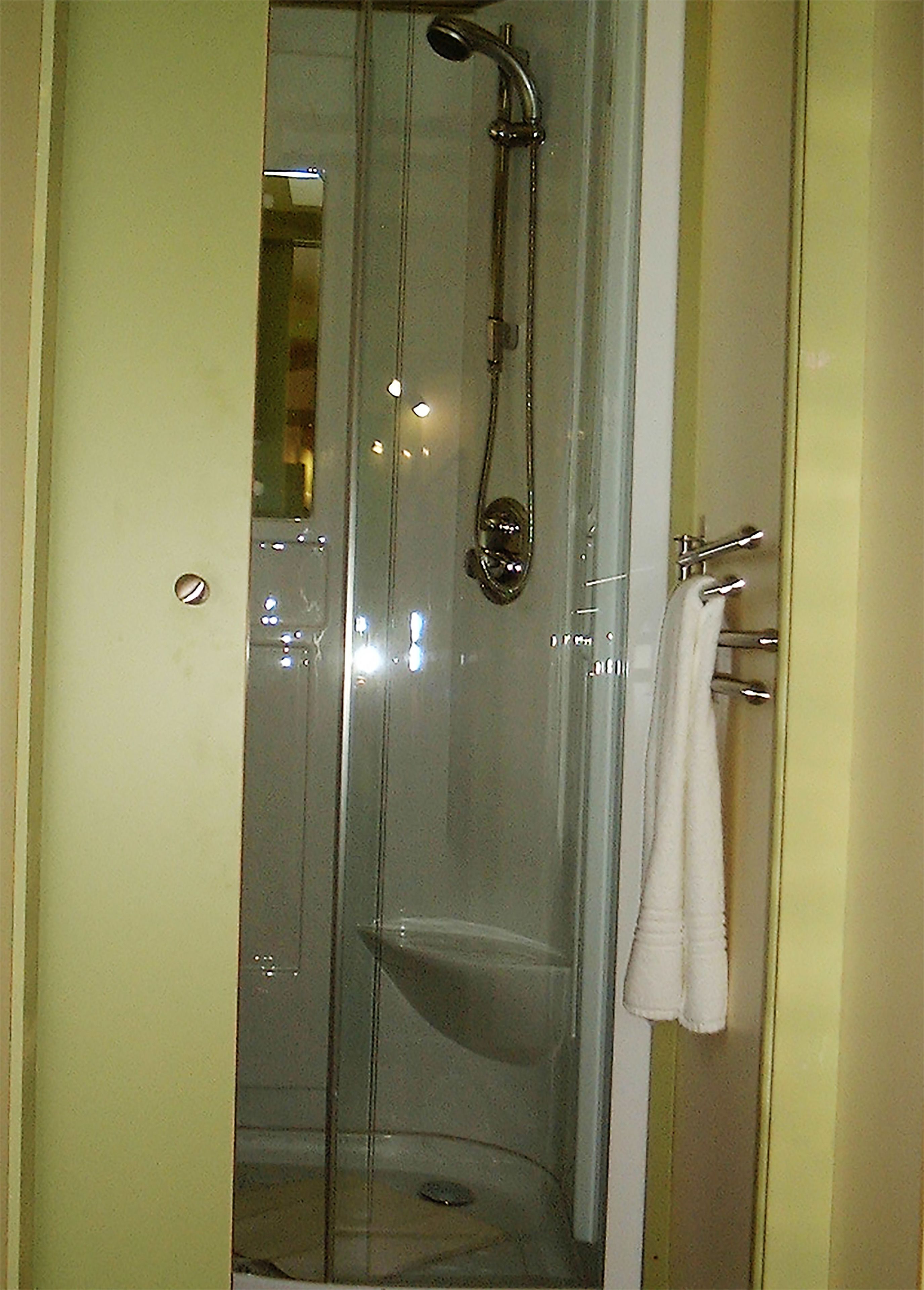 A glass-enclosed shower stall with a handheld showerhead and a towel rack with a towel.