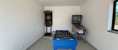 A room with a foosball table, a dartboard, and a television screen displaying a movie.