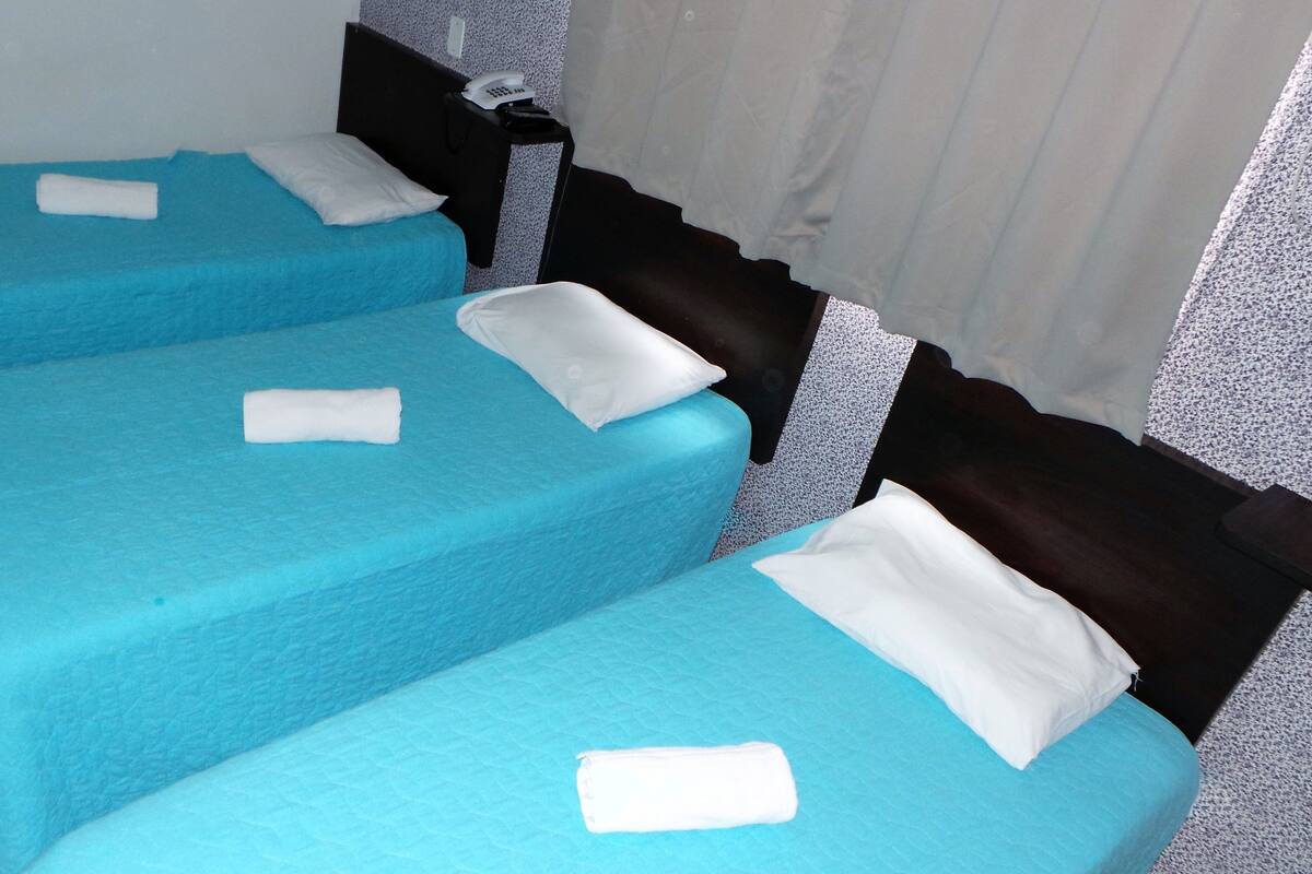 Three single beds with blue bedding and white pillows, a dark headboard, and a telephone on a side table.
