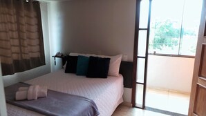 A bedroom with a bed, pillows, a bedside table with a phone, and a window with a view of greenery.
