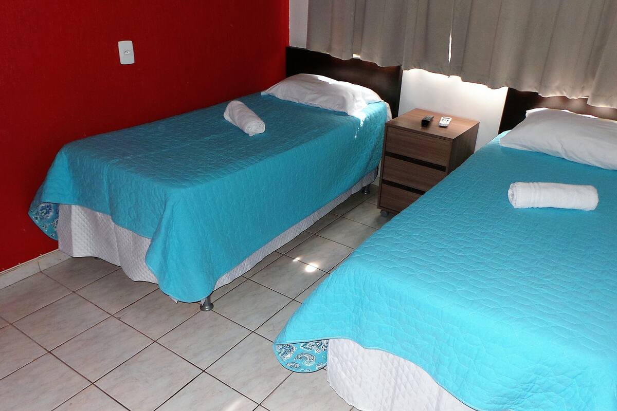 Two single beds with blue bedding, a wooden nightstand, and a red wall.