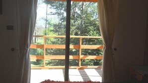 A room with a large window, wooden balcony railing, and a bed with a red blanket. - Cabaña Fau Wualmapu (Pucón)